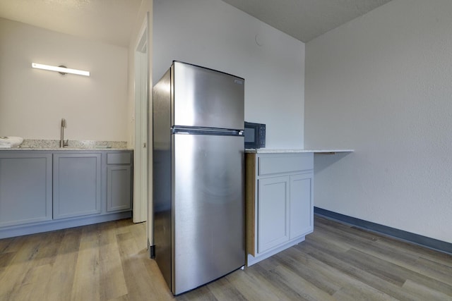 kitchen with sink, white cabinets, stainless steel fridge, and light hardwood / wood-style flooring