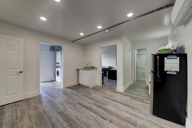 kitchen with stainless steel fridge, a wall unit AC, white cabinets, light hardwood / wood-style flooring, and sink