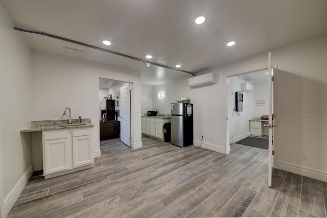 kitchen with white cabinets, wood-type flooring, stainless steel fridge, light stone counters, and a wall mounted air conditioner