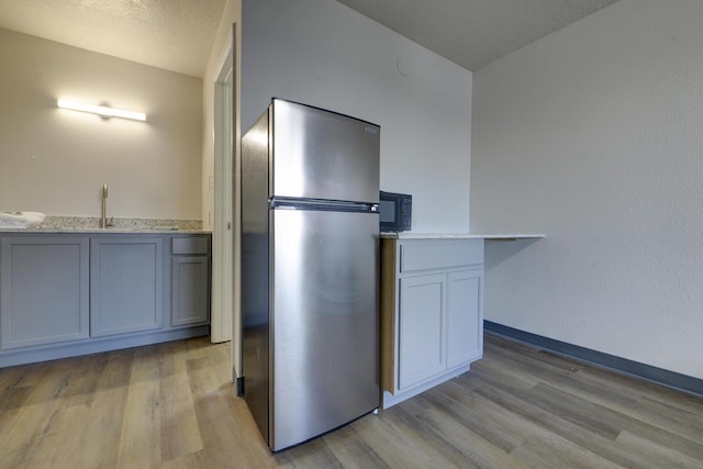 kitchen featuring a textured ceiling, white cabinets, light hardwood / wood-style floors, sink, and stainless steel refrigerator