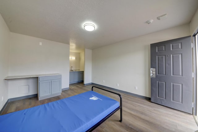 bedroom featuring built in desk, sink, a textured ceiling, and light hardwood / wood-style floors