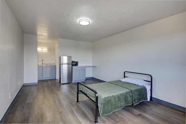 bedroom featuring a textured ceiling, connected bathroom, hardwood / wood-style floors, and stainless steel refrigerator