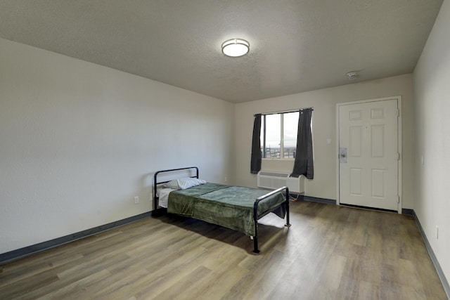 bedroom featuring hardwood / wood-style flooring, a textured ceiling, and a wall mounted air conditioner