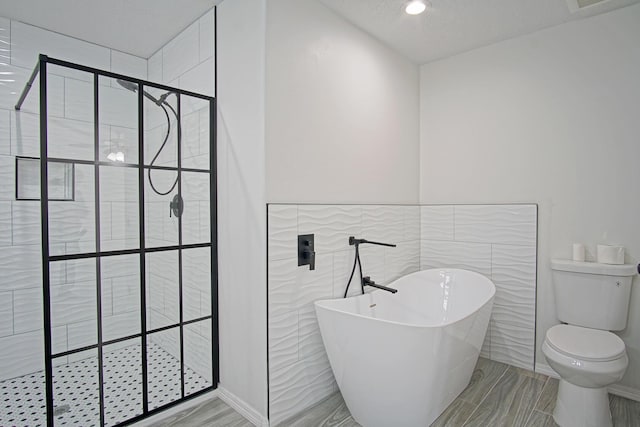 bathroom featuring toilet, a textured ceiling, tile walls, and plus walk in shower