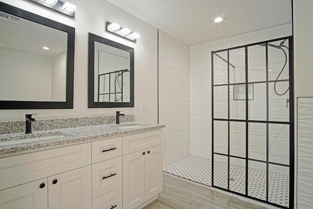 bathroom with vanity, tiled shower, and a textured ceiling