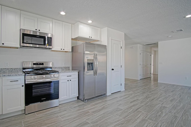 kitchen with light stone countertops, stainless steel appliances, and white cabinetry