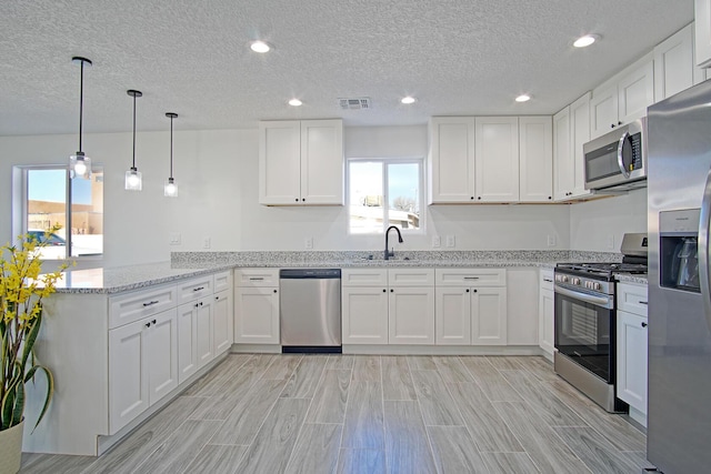 kitchen with kitchen peninsula, stainless steel appliances, light stone countertops, white cabinets, and sink