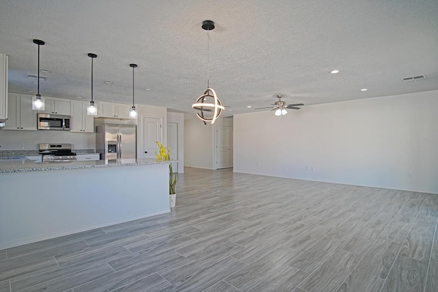 kitchen with light stone counters, white cabinetry, pendant lighting, and stainless steel appliances