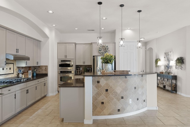 kitchen with a kitchen island with sink, hanging light fixtures, backsplash, and appliances with stainless steel finishes