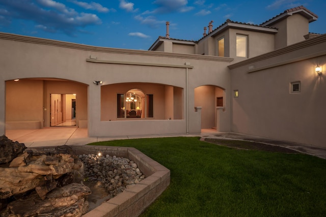 back house at dusk with a lawn and a patio