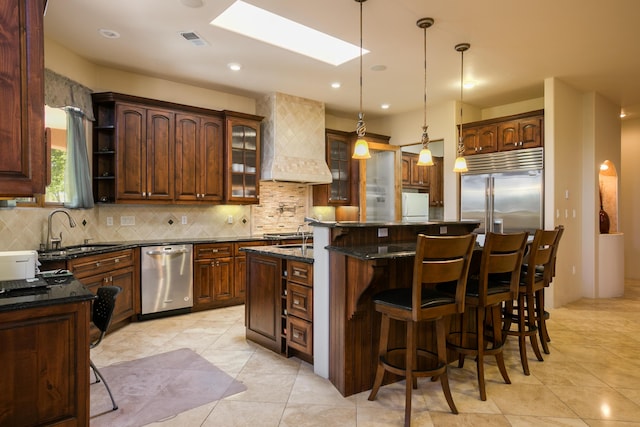 kitchen with premium range hood, appliances with stainless steel finishes, decorative light fixtures, a kitchen island, and sink