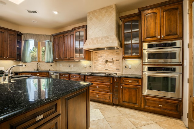 kitchen with premium range hood, sink, appliances with stainless steel finishes, light tile patterned floors, and dark stone counters