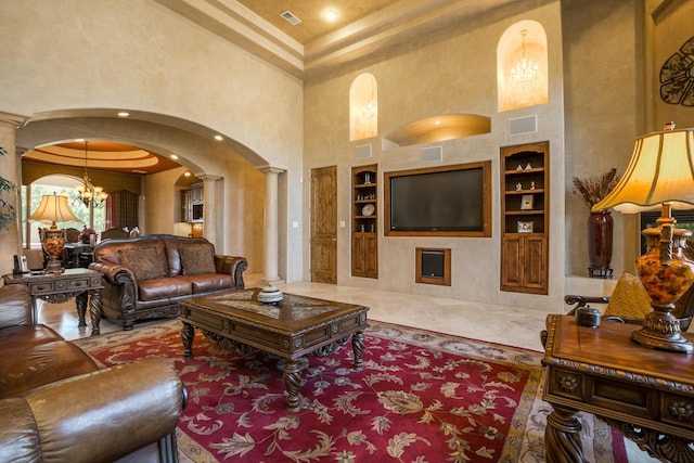 living room with decorative columns, a chandelier, a towering ceiling, and built in shelves