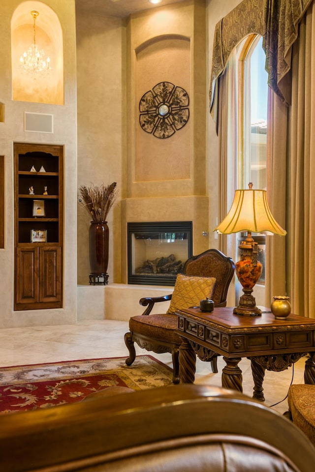 sitting room with built in shelves, a fireplace, a high ceiling, and a chandelier