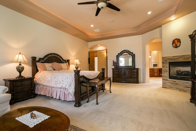 bedroom with ceiling fan, light colored carpet, a raised ceiling, and a fireplace