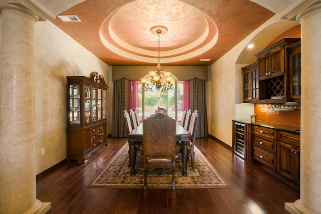 dining area with a notable chandelier, beverage cooler, a tray ceiling, and decorative columns