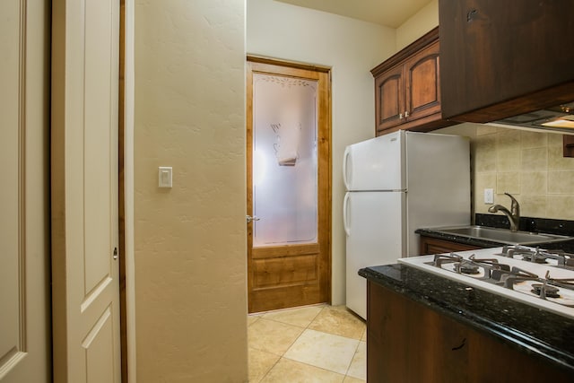 kitchen featuring light tile patterned floors, tasteful backsplash, dark stone countertops, cooktop, and sink