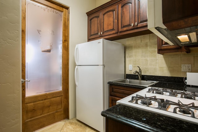 kitchen featuring tasteful backsplash, white fridge, sink, light tile patterned flooring, and dark stone counters