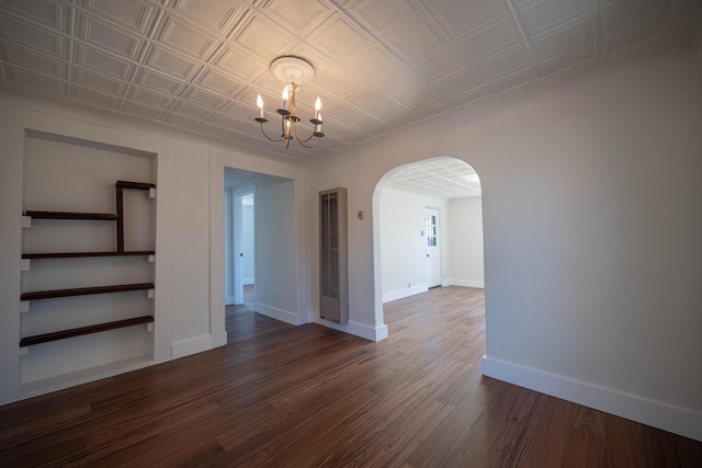 empty room with dark wood-type flooring and a notable chandelier