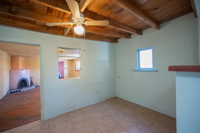 empty room with ceiling fan, light tile patterned floors, wood ceiling, and beam ceiling