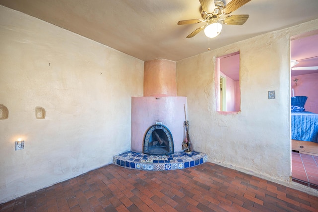 unfurnished living room with ceiling fan and a tiled fireplace