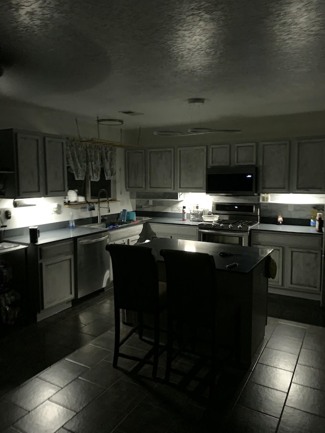 kitchen with stainless steel appliances, a kitchen island, sink, and a textured ceiling