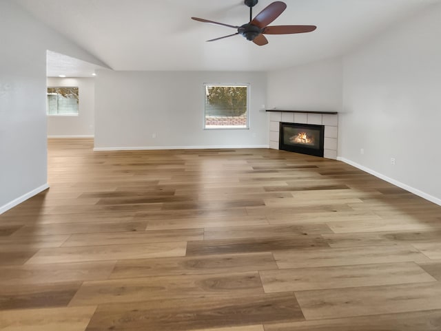 unfurnished living room featuring a tiled fireplace, light hardwood / wood-style flooring, vaulted ceiling, and ceiling fan