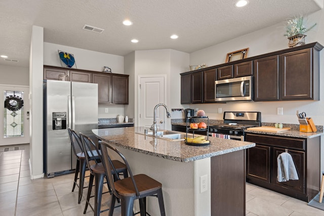 kitchen featuring sink, stainless steel appliances, dark brown cabinetry, an island with sink, and light tile patterned flooring