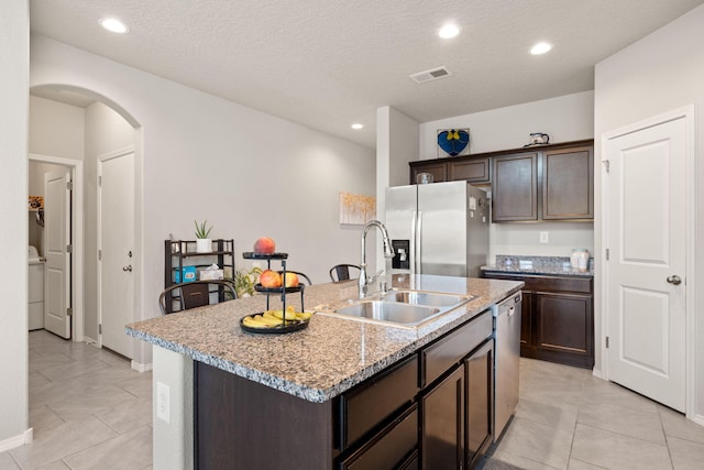 kitchen featuring sink, appliances with stainless steel finishes, dark brown cabinetry, a center island with sink, and light tile patterned flooring