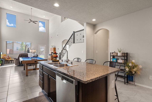 kitchen with sink, light tile patterned floors, a kitchen island with sink, dark brown cabinets, and stainless steel dishwasher