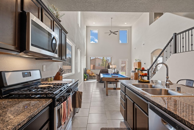 kitchen featuring light tile patterned flooring, dark brown cabinetry, sink, dark stone counters, and stainless steel appliances