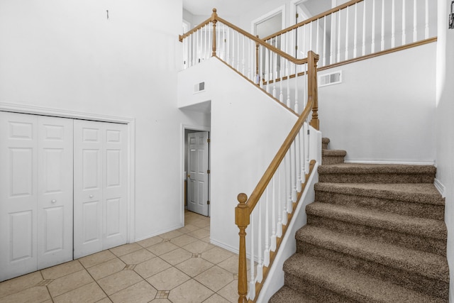 stairs with a towering ceiling, baseboards, visible vents, and tile patterned floors