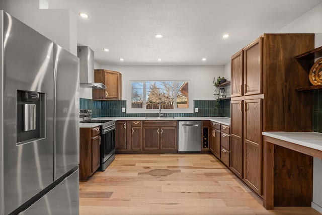 kitchen featuring sink, decorative backsplash, wall chimney exhaust hood, stainless steel appliances, and light hardwood / wood-style flooring