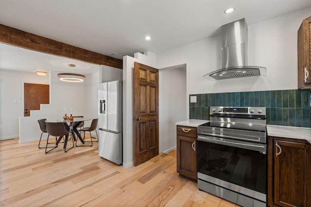 kitchen with appliances with stainless steel finishes, dark brown cabinets, wall chimney exhaust hood, tasteful backsplash, and beamed ceiling