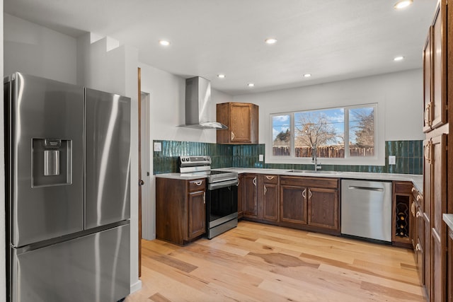 kitchen featuring wall chimney range hood, sink, backsplash, stainless steel appliances, and light hardwood / wood-style floors