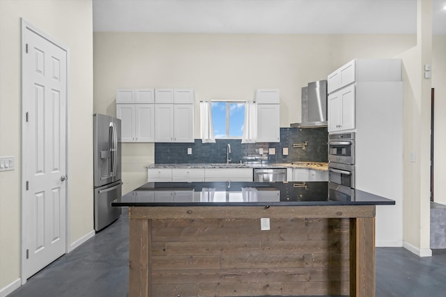 kitchen with wall chimney exhaust hood, sink, white cabinetry, tasteful backsplash, and stainless steel appliances