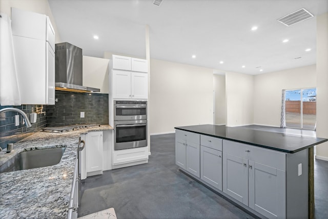 kitchen with sink, white cabinets, wall chimney range hood, a kitchen island, and stainless steel appliances