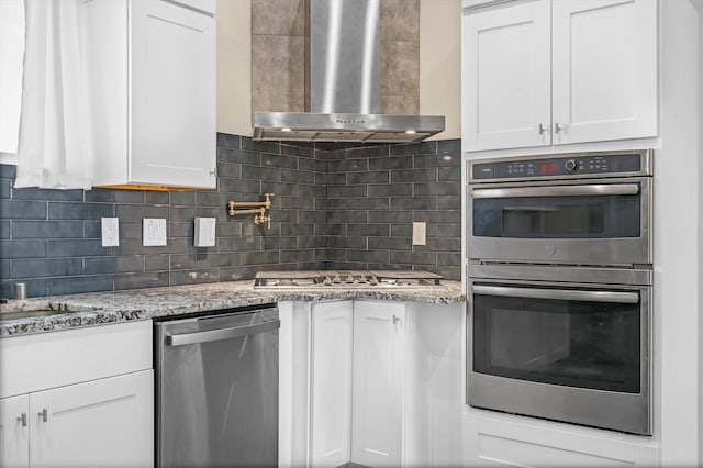 kitchen with wall chimney exhaust hood, white cabinets, and stainless steel appliances