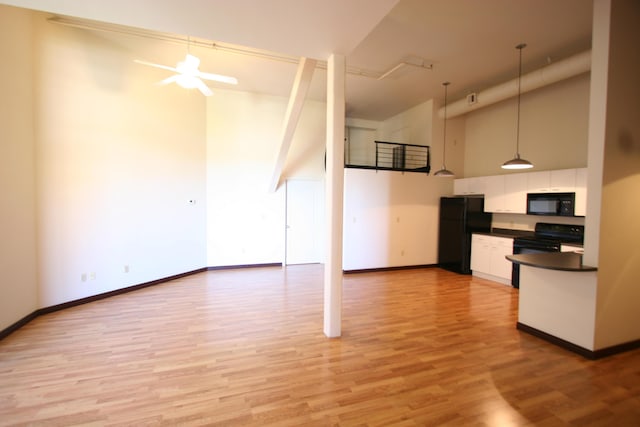 kitchen featuring black appliances, a towering ceiling, light wood-type flooring, and decorative light fixtures