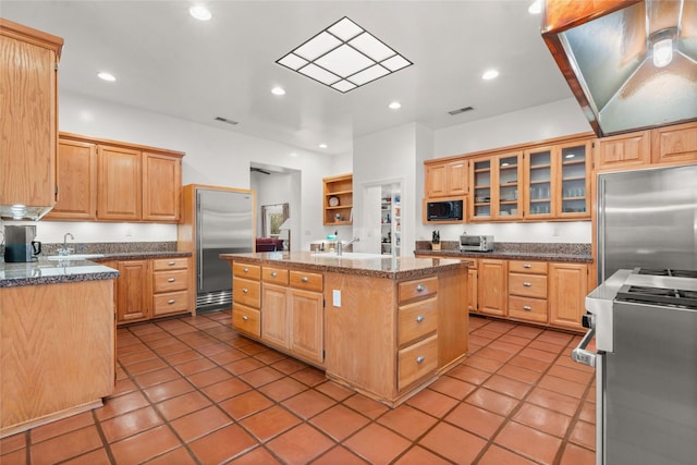 kitchen with light brown cabinetry, an island with sink, and built in appliances