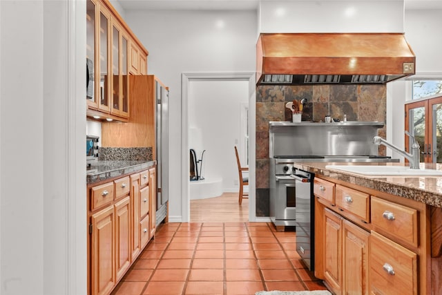 kitchen with custom exhaust hood, decorative backsplash, light tile patterned flooring, stone countertops, and sink