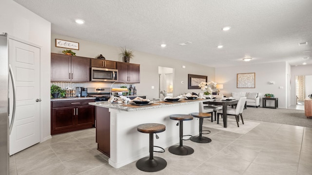 kitchen featuring appliances with stainless steel finishes, backsplash, a kitchen breakfast bar, dark brown cabinetry, and an island with sink