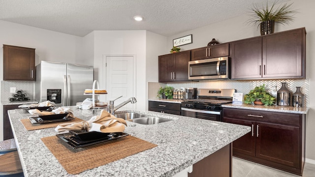 kitchen with an island with sink, appliances with stainless steel finishes, sink, and dark brown cabinets