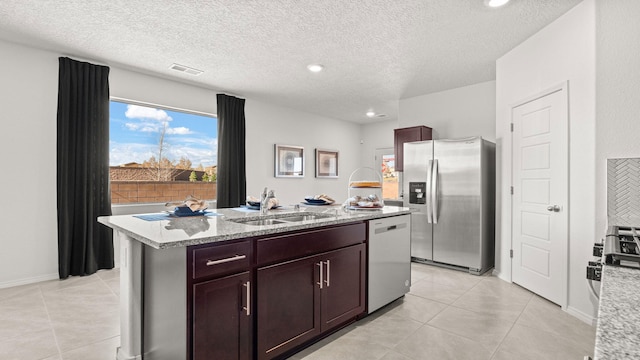 kitchen with light tile patterned flooring, appliances with stainless steel finishes, sink, a kitchen island with sink, and light stone counters