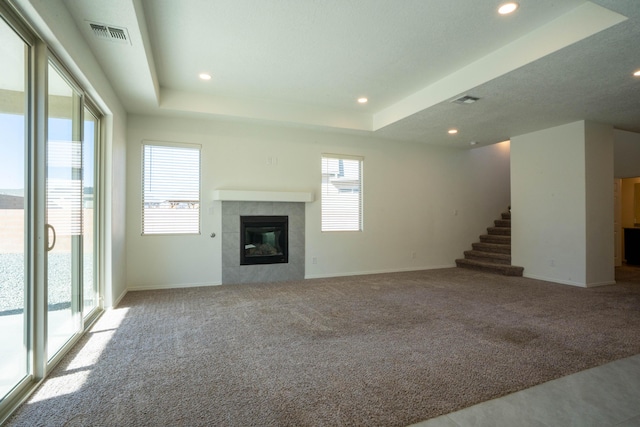 unfurnished living room featuring a tray ceiling, light carpet, and a tiled fireplace