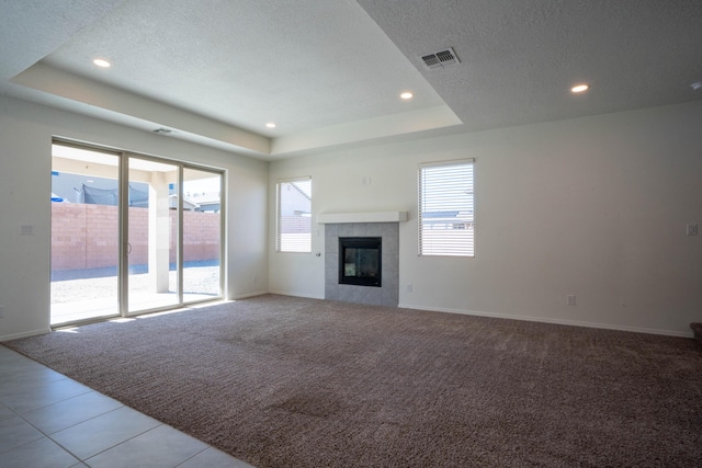 unfurnished living room with light colored carpet, a textured ceiling, a tray ceiling, and a fireplace