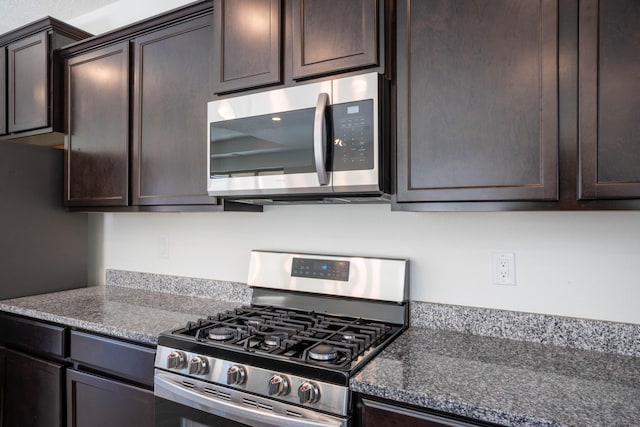 kitchen featuring appliances with stainless steel finishes, dark brown cabinets, and dark stone countertops