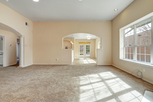 unfurnished living room featuring light carpet, french doors, and decorative columns