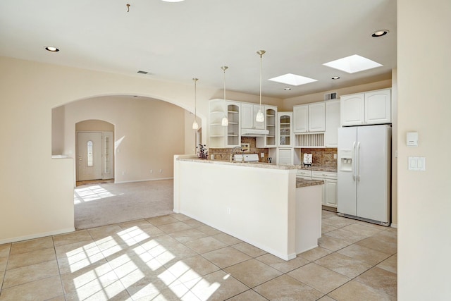 kitchen with tasteful backsplash, white fridge with ice dispenser, white cabinets, kitchen peninsula, and light colored carpet