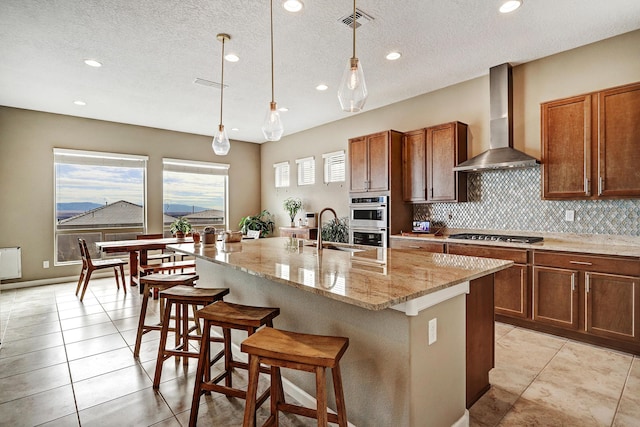 kitchen with light stone counters, stainless steel appliances, tasteful backsplash, visible vents, and wall chimney exhaust hood